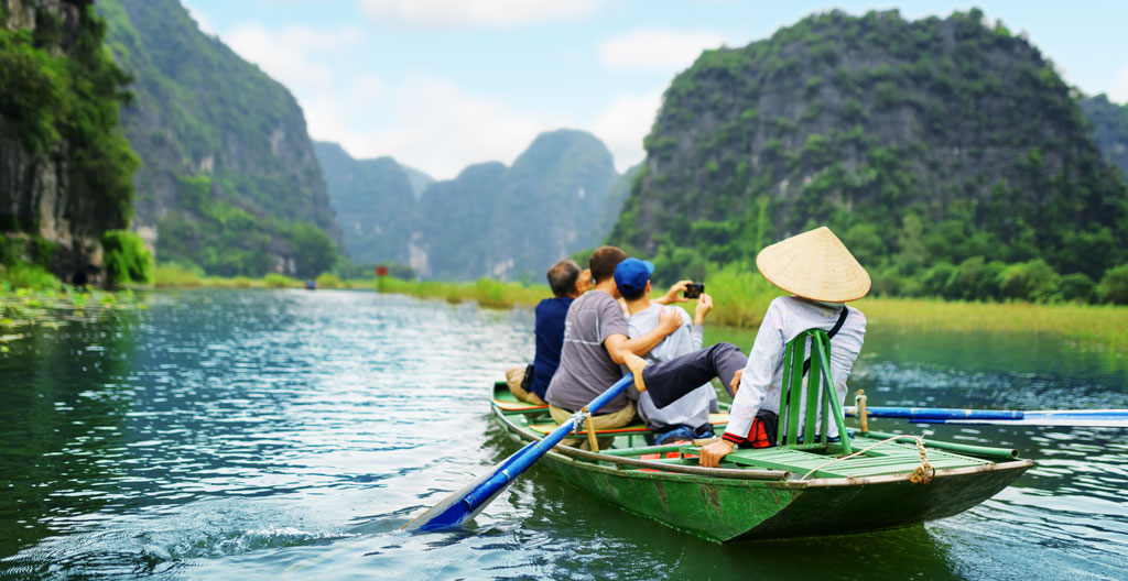 Guide local vietnamien présentant une carte des régions du Vietnam à des voyageurs français dans un bureau d'agence à Hanoï
